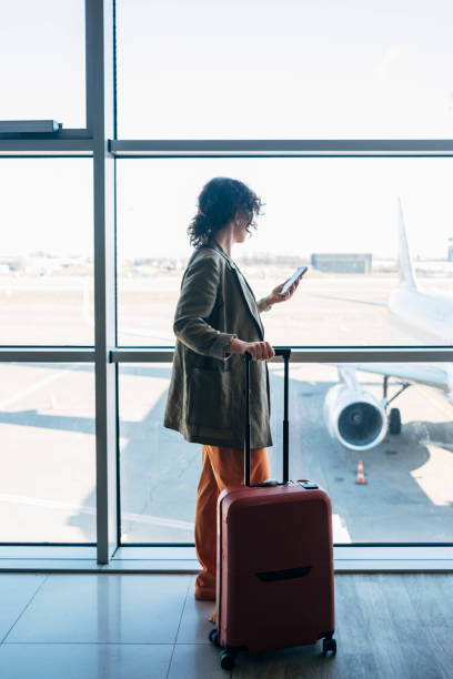 eine seitenansicht einer unkenntlich beschäftigten, eleganten geschäftsfrau, die ihr mobiltelefon benutzt, um mit ihren geschäftspartnern zu sprechen, während sie auf ihren flug wartet - pre flight stock-fotos und bilder