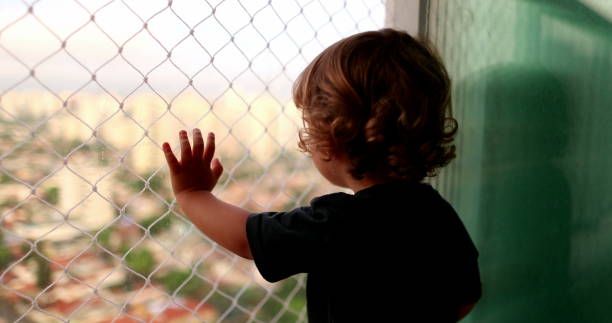 Baby child hand leaning on window balcony with safety net stock photo