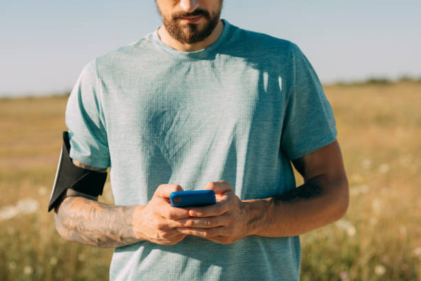 istock Unrecognizable White Runner Standing in the Meadow and Using his Mobile Phone 1387111121