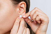 Cropped shot of a young woman wearing elegant diamond earrings on a gray background. Jewelry concept