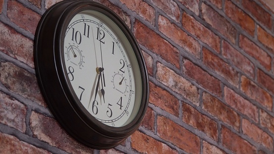 Wall clock with a light dial. Retro style. The movement of time. Temperature and humidity indicators. Round form. Dark frame. Brick wall. Close-up.