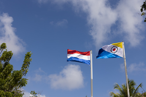 Flag of Bonaire and Netherlands flying in the wind on the blue sky background