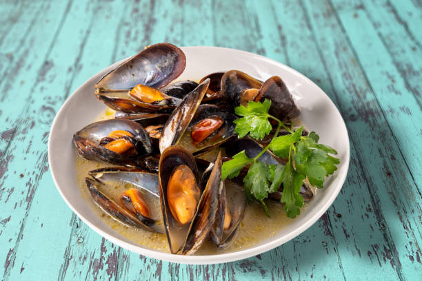 Mussels cooked with an Italian recipe called tarantina mussels Mussels cooked with an Italian recipe called tarantina mussels in white, in a plate with parsley on rustic blue wooden table taranto stock pictures, royalty-free photos & images