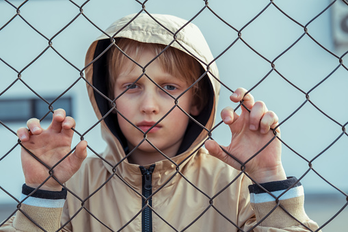Sad boy standing behind grid fence