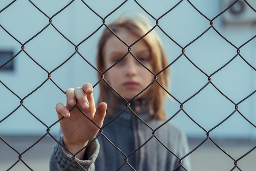 Sad girl standing behind grid fence