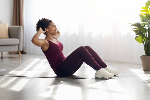 Cheerful african american woman exercising on fitness mat at home Cheerful millennial african american woman in sportswear exercising on fitness mat at living room alone, doing crunches, working on abs, looking at copy space and smiling, side view. Sport at home sit ups stock pictures, royalty-free photos & images