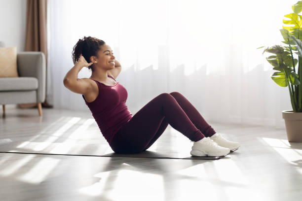 wesoła afroamerykanka ćwicząca na macie fitness w domu - sit ups zdjęcia i obrazy z banku zdjęć