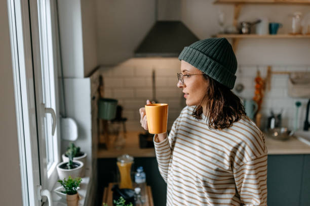 Woman with coffee cup looking through window at home stock photo