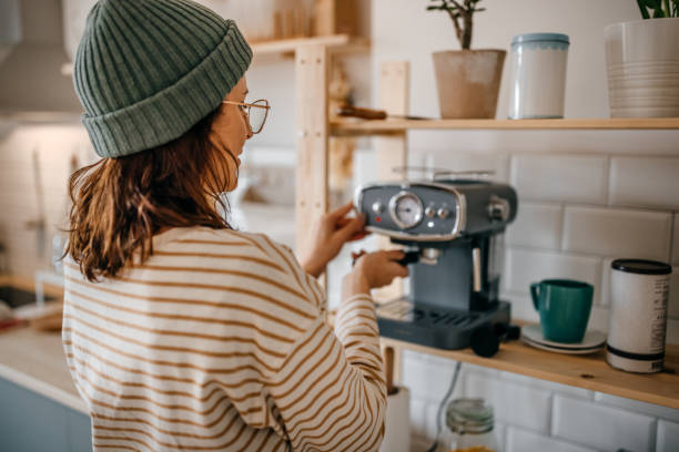 женщина готовит кофе через машину на кухне - machine made стоковые фото и изображения