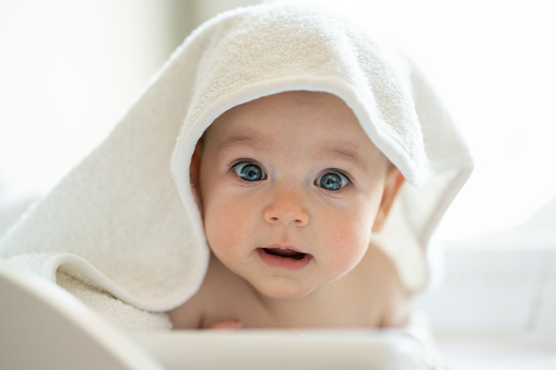 Cute baby wearing towel after bath and looking at camera