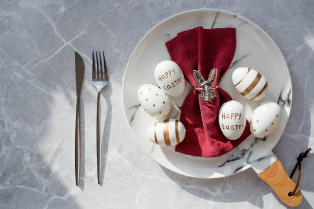 istock Banner. Table setting. A fashionable marble plate with a rabbit on a napkin, Easter eggs and feathers on a gray background. Top view. Happy Easter holiday concept for cafes and restaurants. 1387125297