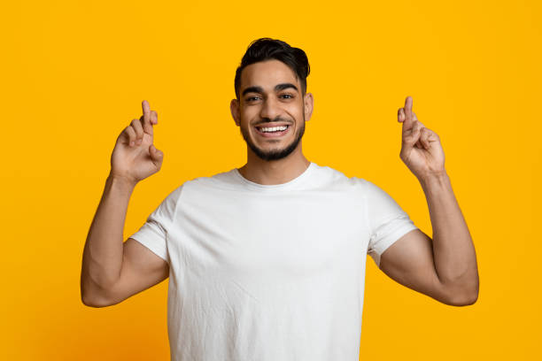 istock Positive middle eastern guy showing fingers crossed and smiling 1387126070