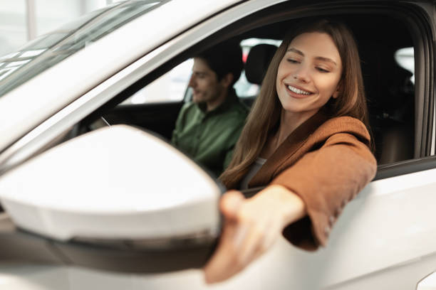 istock Happy young woman with her husband sitting inside new car, checking it before purchase at modern dealership store 1387126725