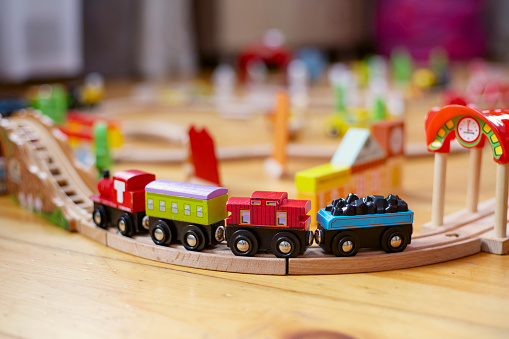 Wooden toy train on railroad with brick town on floor. Toys for kids indoor.