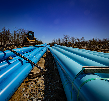 Bright blue sewer pipes unloaded on construction site in front of motorized equipment.