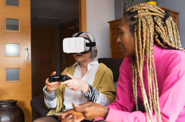 istock Older woman playing with a console and virtual reality goggles sitting on the sofa next to a girl 1387128865