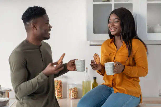 Photo of Couple's Leisure. Happy Black Spouses Drinking Coffee With Cookies In Cozy Kitchen