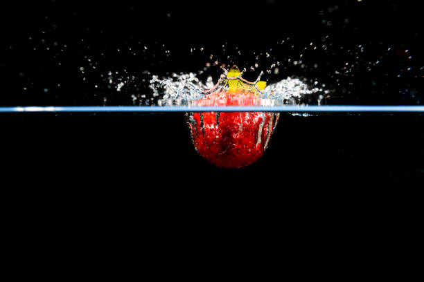 One fresh green juicy lime is falling into crystal clear water. There are splashes of water and bubbles rising high above the lime from where it broke the waters surface. The fruit and splashes are isolated on a white background with a clipping path.