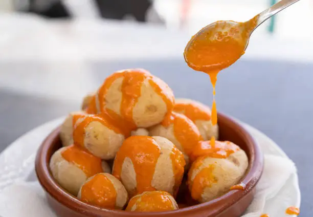 Photo of Spoon pouring spicy mojo sauce on papas arrugadas in clay plate