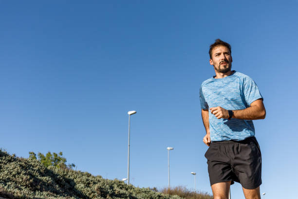 istock caucasian millennial man running in a sunny day, blue sky background 1387131259