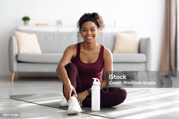 Positive Sporty Black Lady Sitting On Fitness Mat And Smiling Stock Photo - Download Image Now