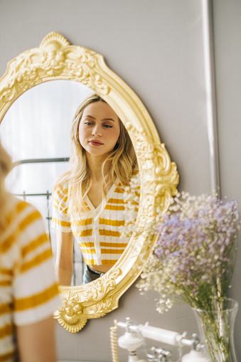 Young attractive caucasian woman looking in the mirror at her face, beauty treatment, skin care concept.