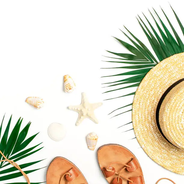 Photo of Woman's beach accessories flat lay. Straw hat, leather sandals, tropical palm leaves, seashells, starfish on white background. Top view copy space. Summer backdrop
