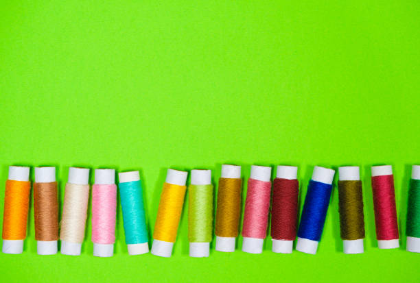 A set of multi-colored threads for sewing with an empty space for text on a green background, top view. Tailoring and needlework equipment, tailor banner