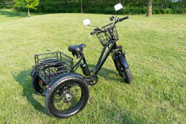 Electric trike or bicycle in the park in sunny summer day. Unfiltered, with natural lighting. E motor and power battery of the three wheel bike. Ecology and green energy concept. Ev – electric vehicle