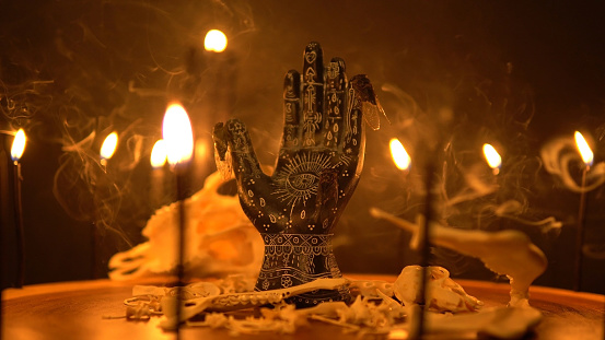Black fortune teller hand with constellations on the reader table with magic animal bones, goat skull and cicada insects. Alchemy spirituality symbolic background with candle smoke and fog.