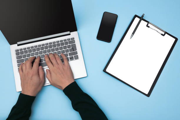 istock Directly above view of human hands typing on laptop at workplace on blue surface for mockup. 1387136510