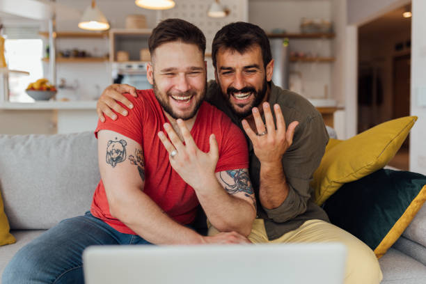 Engagement Young happy gay couple in love just got married so they have a video call with their friends and family to spread the joy. The couple showing their wedding rings. civil partnership stock pictures, royalty-free photos & images