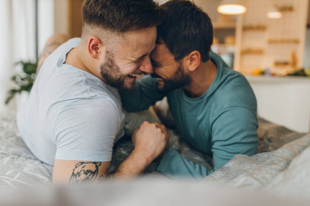 schwulenpaar liegt im bett und umarmt - homosexuelles paar stock-fotos und bilder