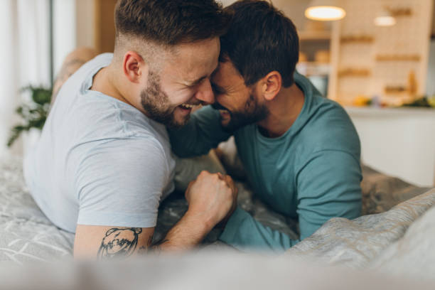 Gay couple lying in bed and hugging Happy gay couple lying in bed and hugging. homosexual couple stock pictures, royalty-free photos & images