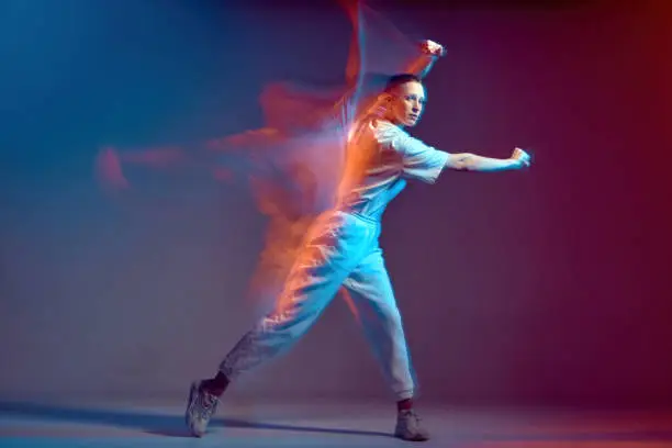 Photo of Dancing modern energetic sports girl moving, waving hand. Breakdancer in colourful neon studio light. Long exposure