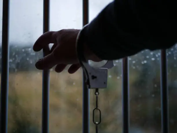 Prisoner in handcuffs reaches through prison bars medium shot selective focus