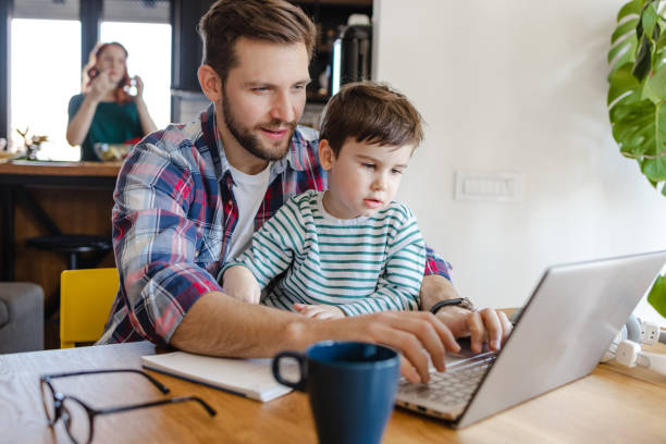 istock Father works on a laptop and holds his son on his lap 1387142066
