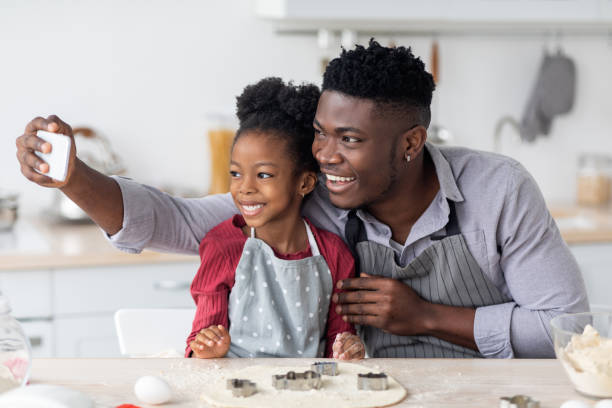 lindo padre e hija negros horneando juntos, tomándose una selfie - hornear fotos fotografías e imágenes de stock