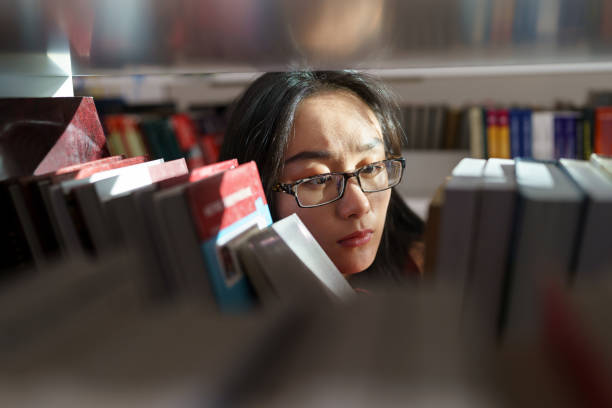 istock Asian girl student looking for book or textbook on library bookshelf studying at university campus 1387144849