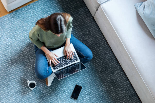 istock Pretty young woman using her laptop while sitting on the floor at home. 1387145789