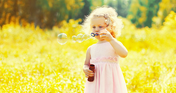 Portrait of little girl child blowing soap bubbles in sunny summer day