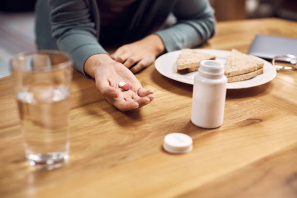 nahaufnahme der frau, die während des frühstücks am esstisch pillen einnimmt. - eating sandwich emotional stress food stock-fotos und bilder