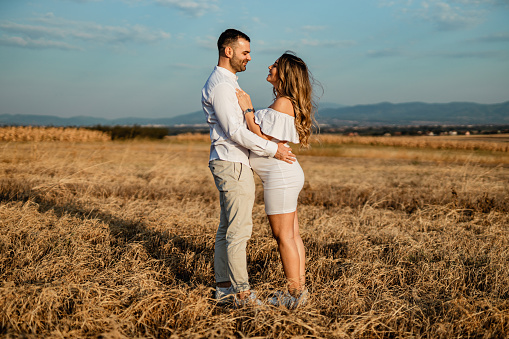 A young pregnant woman and a young man wearing white clothes in nature on a sunny summer day