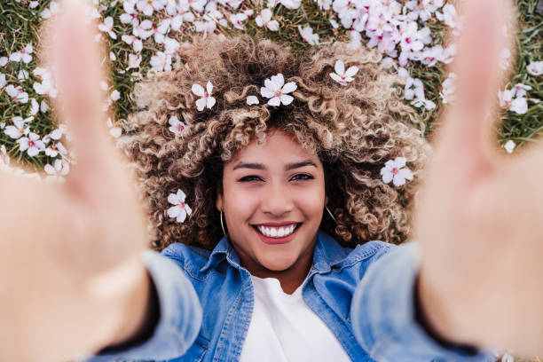top view of happy hispanic woman with afro hair lying on grass among pink blossom flowers.Springtime stock photo