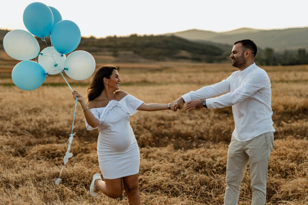 Pregnant couple revealing baby gender with balloons Happy pregnant woman and a man revealing baby gender with blue balloons on a sunny summer day in nature couple hope sky blue stock pictures, royalty-free photos & images