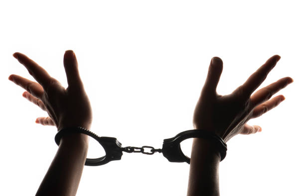istock Female hands silhouette with handcuffs, on the white background. 1387148239