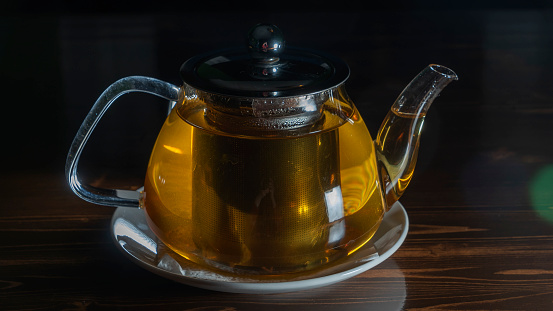 Glass teapot with tea on dark background. Green tea and teapot on wooden table. Advertising composition. Space for text.