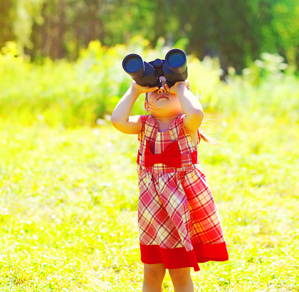 Portrait of little girl child looking through binoculars outdoors in sunny summer day