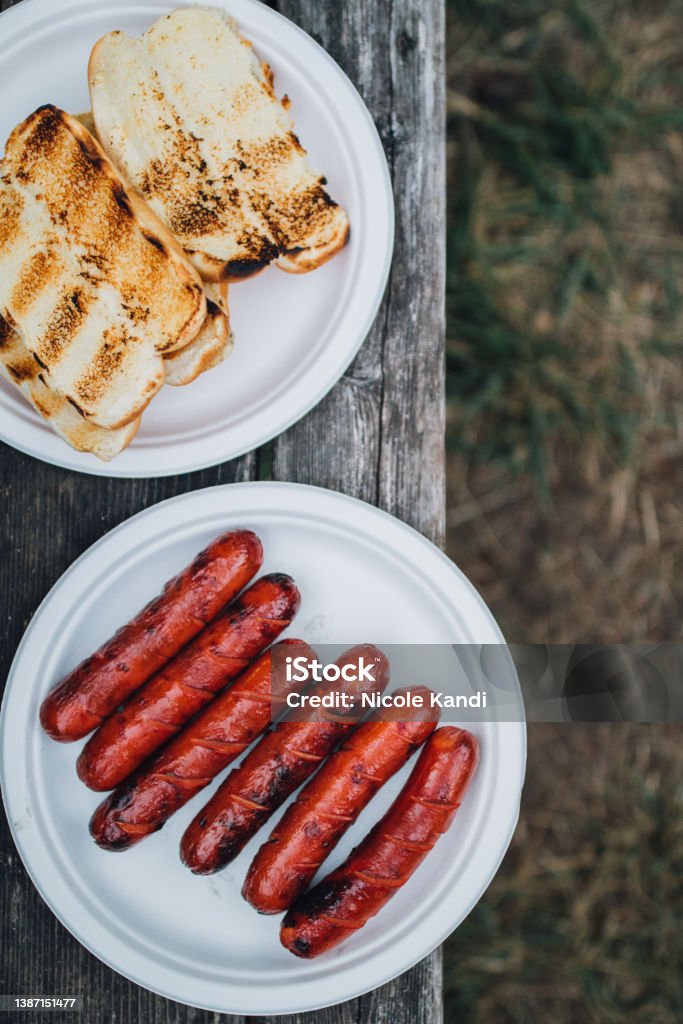 Grilled hotdogs and buns on paper plates six barbecued beef hot dogs on white paper plate on picnic table with pile of grilled buns Hot Dog Stock Photo