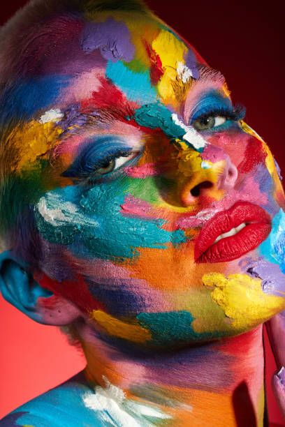 istock Studio shot of a young woman posing with multi-coloured paint on her face 1387152485